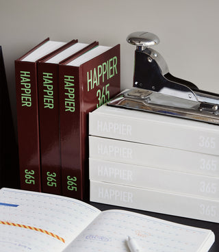 Burgundy Happier 365 diary notebooks stacked with “365” labels and stapler on top.