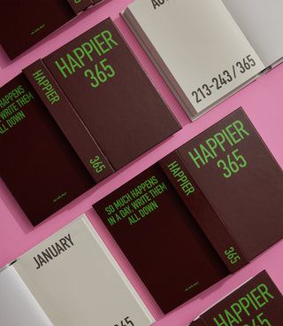 Brown diary notebook with green “Happier 365” title and stitched date ribbon tag.