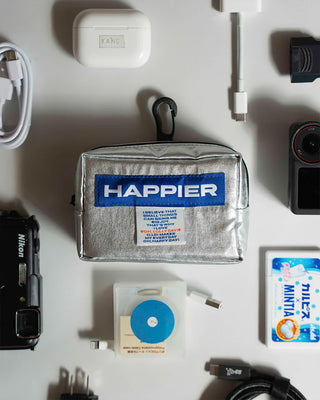 Silver fabric tofu pouch with zipper, black strap, and Happier label