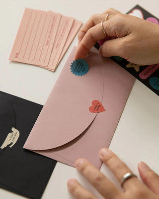 Hand applying pastel motivational stickers to a pink paper envelope flap