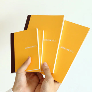Stack of orange A5 graph notebooks with dark side stripes