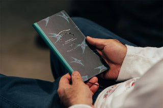 Lucky Swallow-themed 2027 planner with dark cover and teal edge, held in hands.