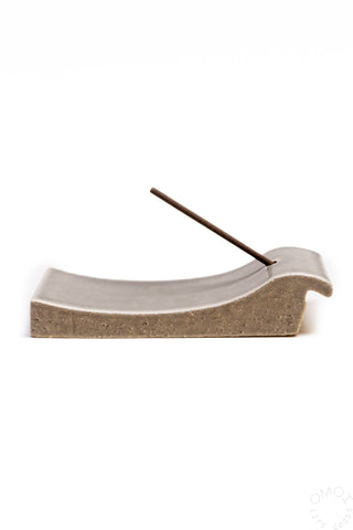 Grey clay incense burner with curved opening and incense stick resting inside