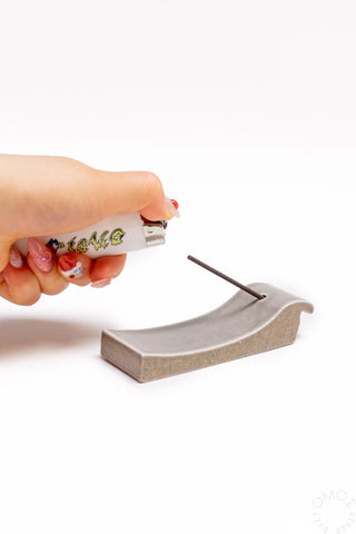 Hand holding incense stick over grey clay incense burner with curved channel