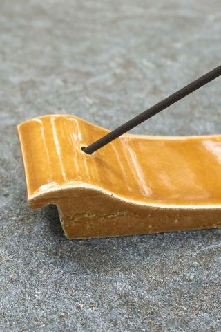 Terracotta incense burner end with black incense stick in holder, glossy orange glazed tray