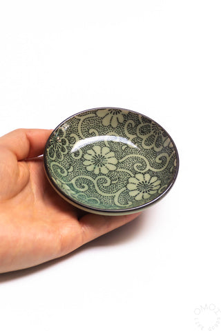 Round ceramic sauce dish with green floral print, held in hand