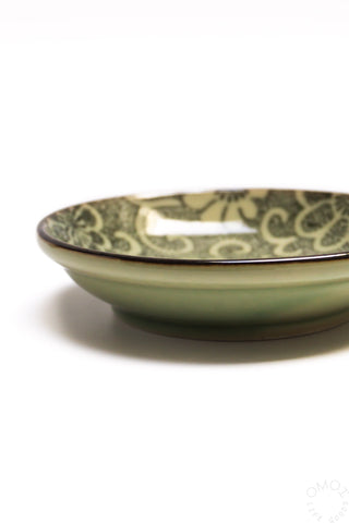 Ceramic sauce dish with green base and floral pattern on rim