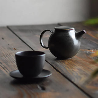 Black pebble-style teapot with curved handle and spout, small cup beside it