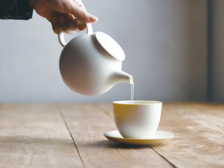 Light-colored teapot pouring hot tea into a white cup