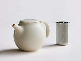 White teapot with lid and handle beside a stainless-steel infuser tumbler