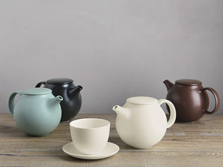 Brown teapot with curved handle and spout on table with two cups