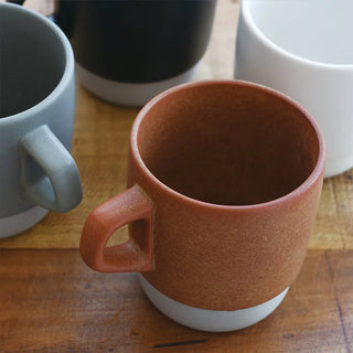 Orange-brown ceramic coffee mug with curved handle and white bottom, close-up