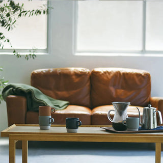 Ceramic mugs in brown and dark teal with side handles, part of a stacking set