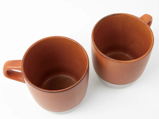 Two ceramic orange coffee mugs, showing interiors and curved handles