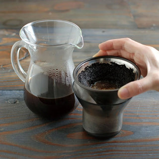 Clear glass carafe and metal cup with coffee grounds on a wooden surface