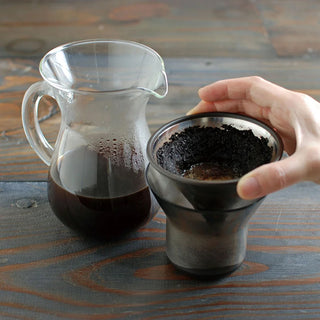 Stainless coffee carafe and reusable filter cone with hand holding grounds cup