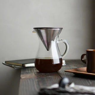 Stainless coffee carafe with pouring spout and glass-like body holding coffee