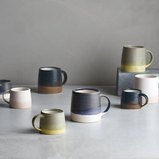 Assorted two-tone ceramic coffee mugs with banded colors and matching handles