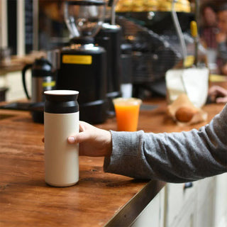 Cream 500ml travel tumbler with black lid on a wooden table
