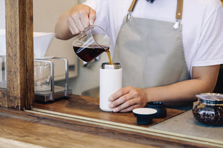 White 500ml travel tumbler with black lid behind the counter