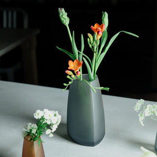 KINTO TRE smoke glass vase holding orange tulip stems with green leaves.