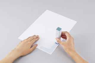 Glue stick applying adhesive to white paper, blue tip