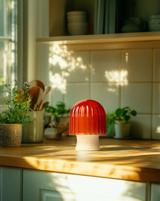 Red and white candle on a wooden kitchen counter with plants and utensils in the background