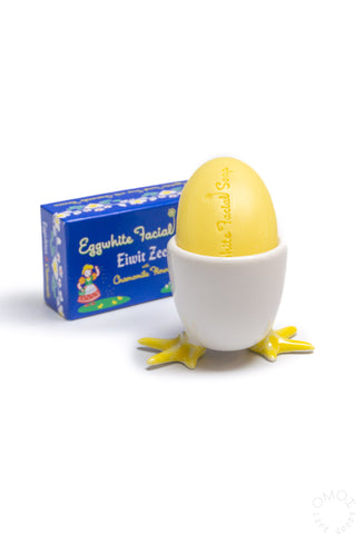 Egg soap cup with white cup, yellow star feet, and yellow egg half beside a blue carton