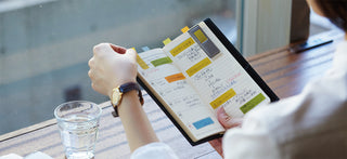 Colored sticky notes and pad clipped on a planner page, held by a hand