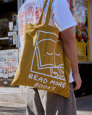 Mustard tote bag with Read More Books print, carried on shoulder with illustration visible.