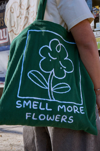 Green tote bag with large embroidered flower and 'SMELL MORE FLOWERS' lettering