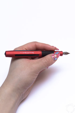 Hand holding a red Kaweco AC Sport fountain pen with black grip and steel nib