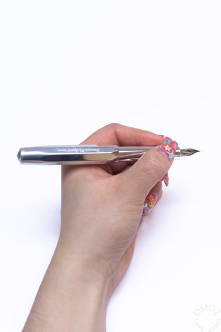 Kaweco AL Sport raw aluminum fountain pen held in hand, steel nib ready to write