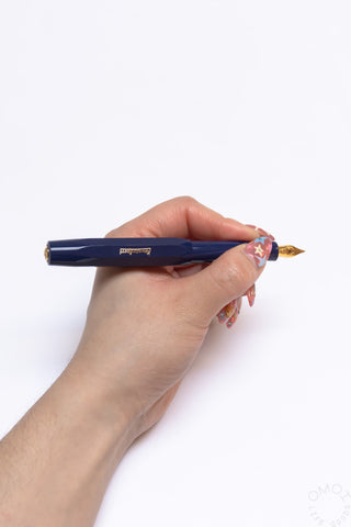 Navy fountain pen held in hand with gold medium nib exposed