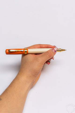 Cream and orange student rollerball pen held in hand, gold clip and tip