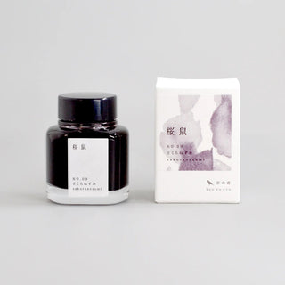 Black glass ink bottle with purple watercolor label and white presentation box.