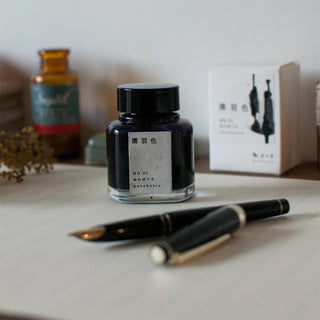 Black glass ink bottle with matching pen and cap on a tabletop.