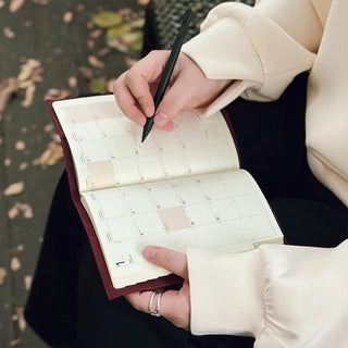 Open olive A5 notebook cover with grid pages, held while writing with a pen