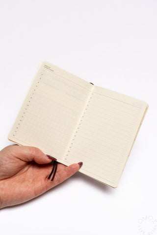 Pocket log diary open to blank lined pages on cream paper; hand points to text area