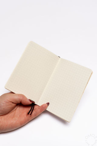 Cream pocket log diary open to dotted pages, hand holding the book