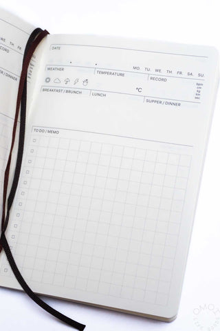 Close-up of cream log diary planner with weather section and grid layout
