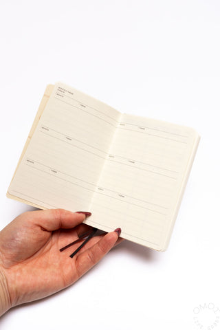 Cream log diary open to lined pages with bookmark ribbon held in hand