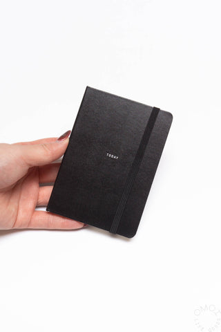 Black B7 pocket log diary with elastic strap, held closed in hand