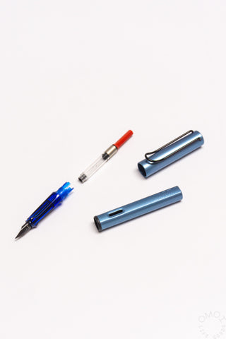 Fountain pen ink converter with red cap beside blue pen body parts