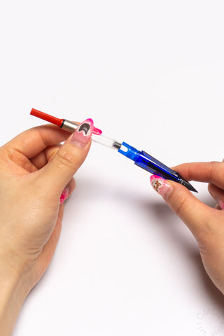 Hands inserting red-capped ink converter into a blue fountain pen
