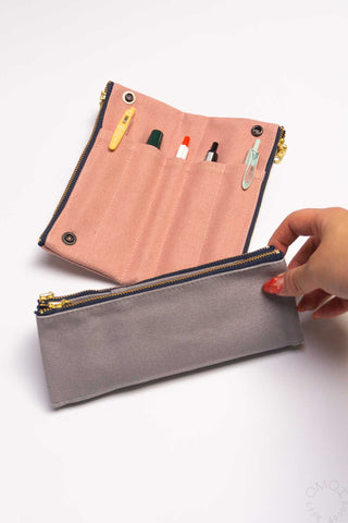 Pink pencil roll with zip flap and grey fold pocket; hand holds open edge