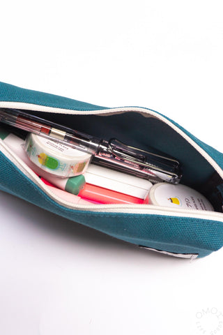 Open teal box pen case interior with pens, markers, and small accessories