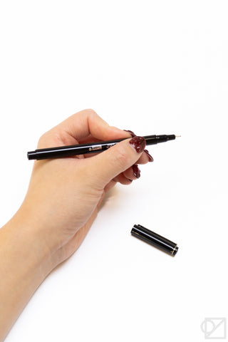 Le Pen fine-tip pen held in hand, dark barrel with colored ink