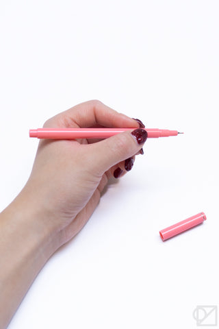 Hand holding a pink pastel gel pen, with a small pink pen piece