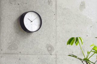 Wall-mounted round clock with white face, black bezel, and minute/hour hands